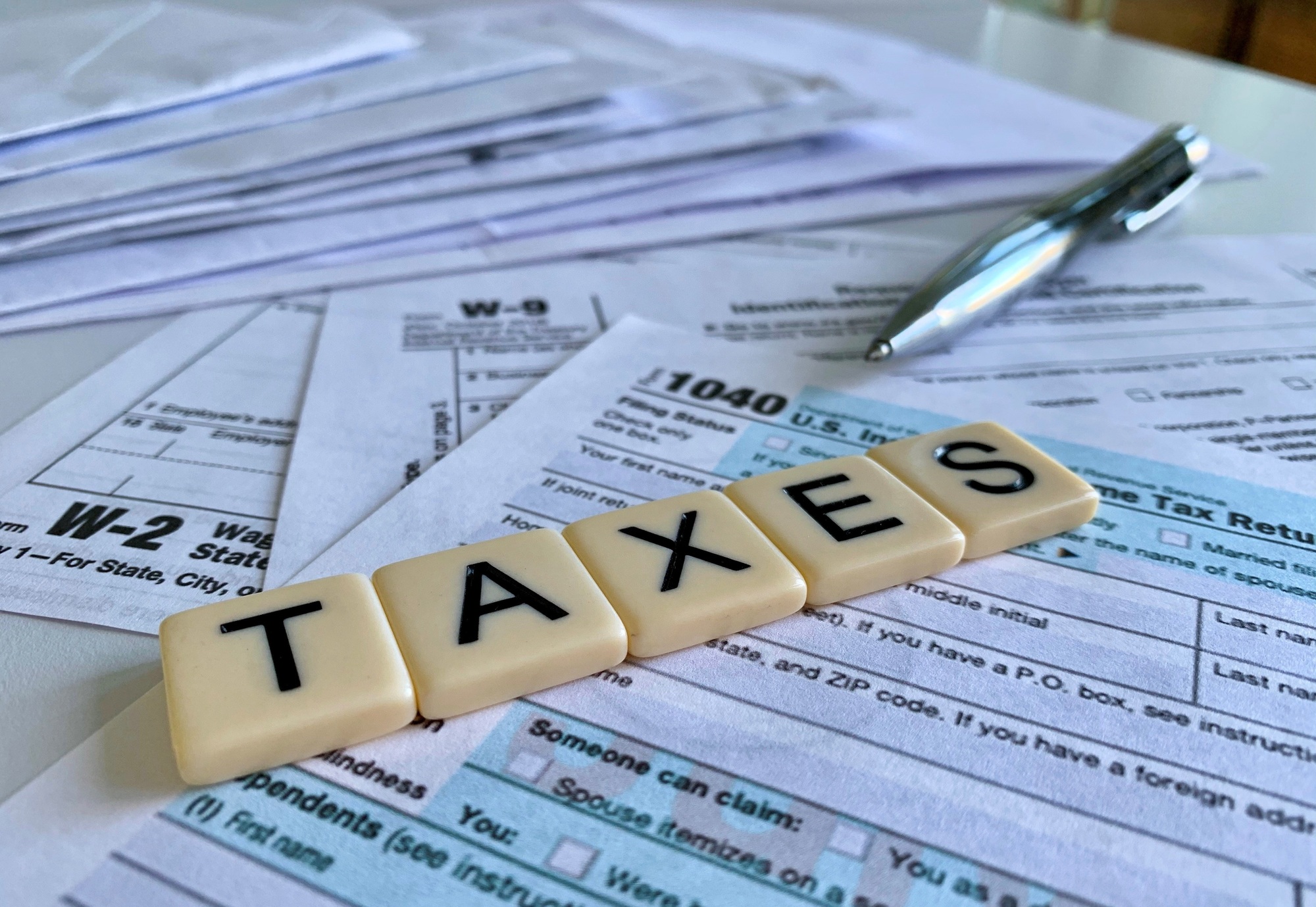 Low angle of letter tiles with the word TAXES on a variety of tax forms.